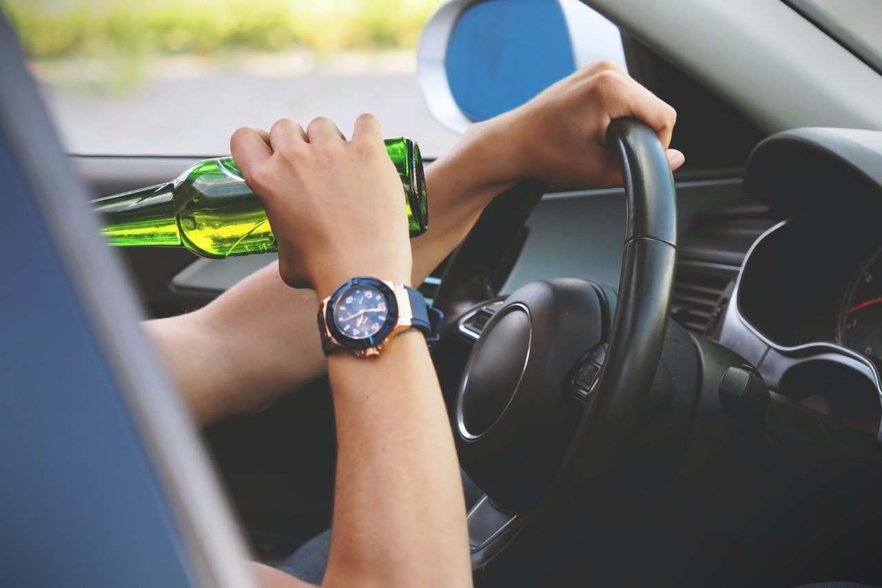 A person drinking a bottled beer while driving