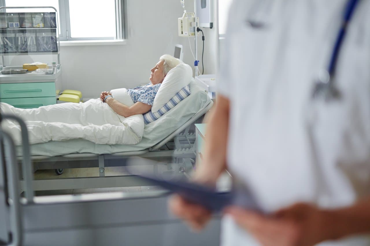 Old woman lying in hospital bed with doctor in foreground