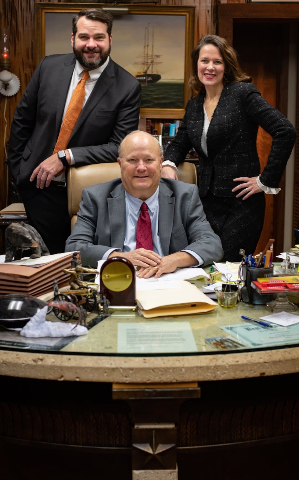 A group of attorneys standing around a table with papers and a man sitting at a desk.