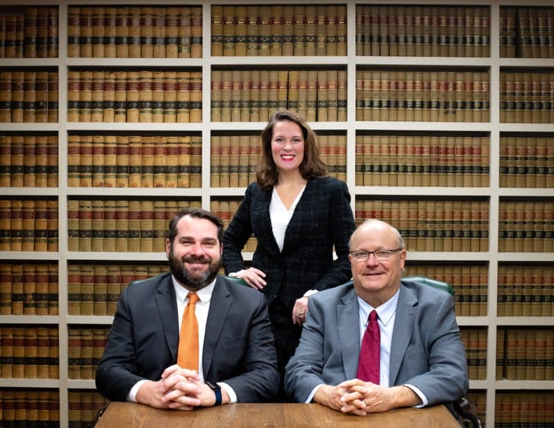 Photos of three attorneys in front of law library books