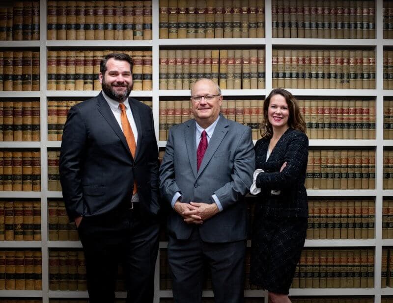Two men and woman standing in front of law books