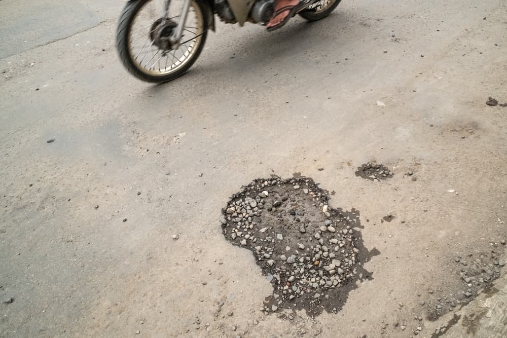 A road with a pothole as motorcycles pass by.